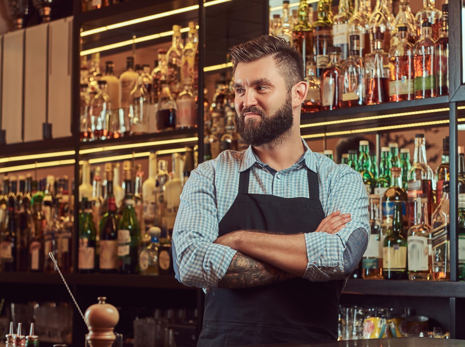 elegante barman brutal camisa delantal pie brazos cruzados fondo mostrador bar 613910 20087